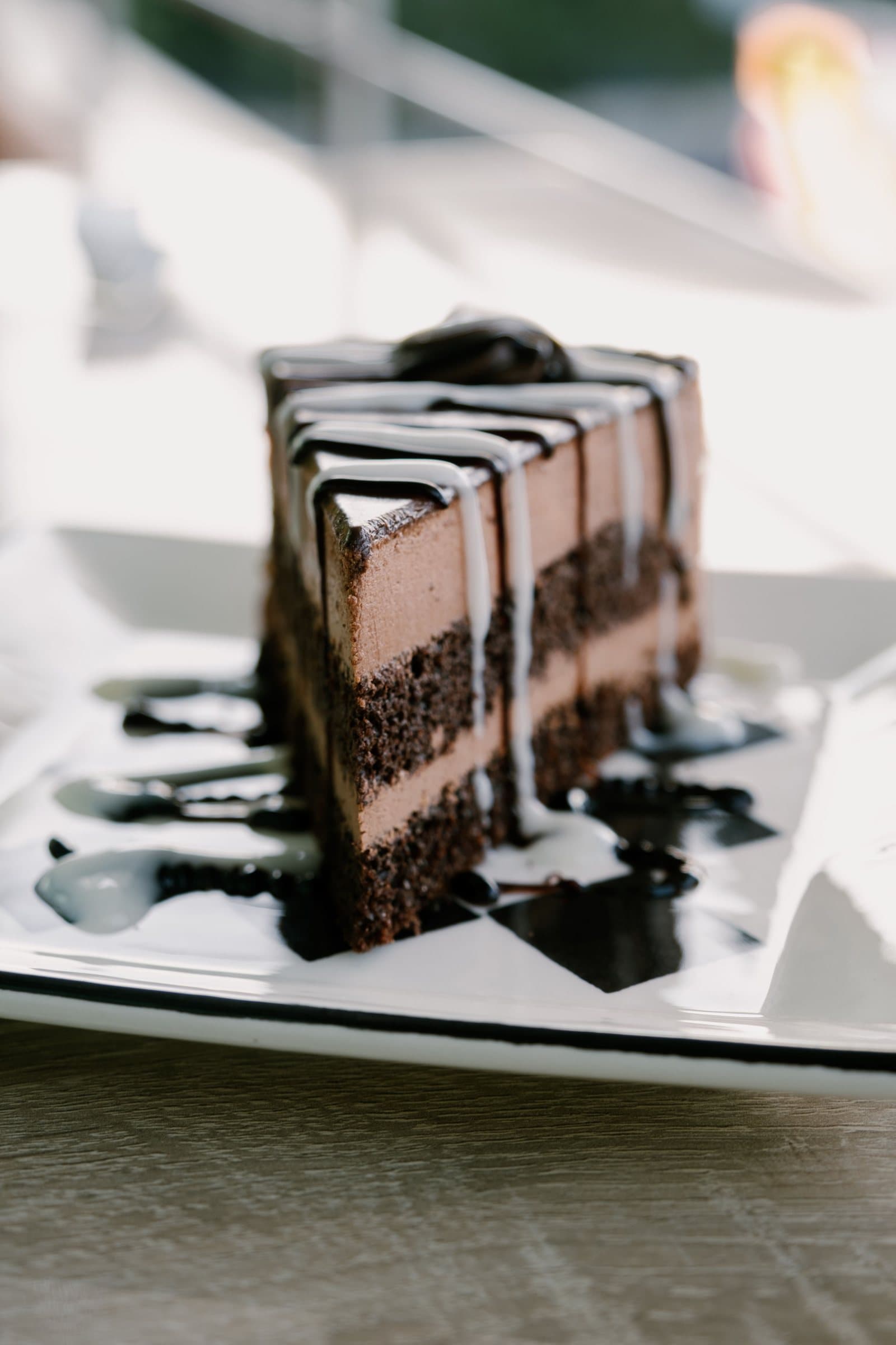 A slice of layered chocolate cake drizzled with chocolate and white glaze on a plate