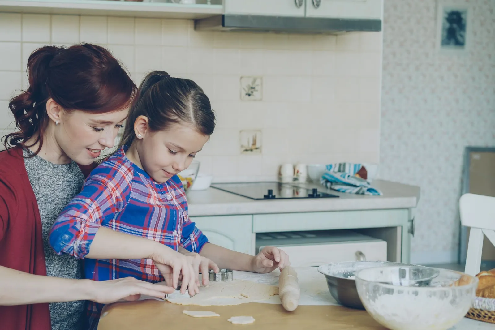A mother and daughter cutting shapes from cookie dough together in a home kitchen