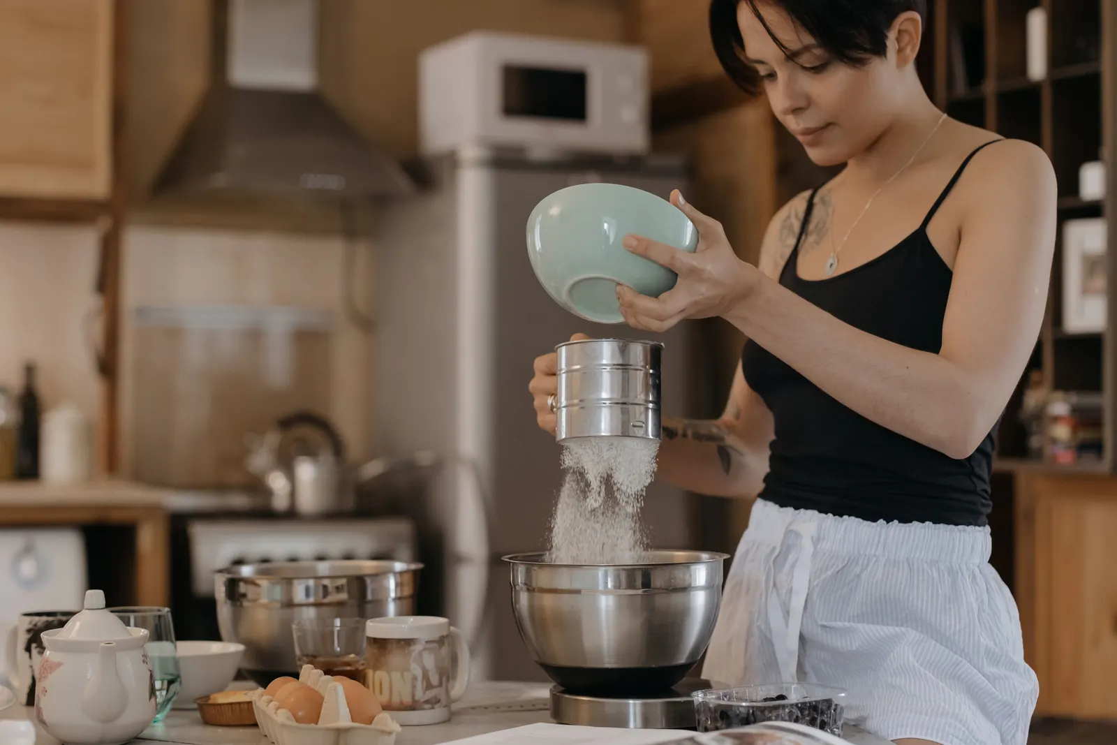 A woman calmly sifting flour into a bowl in a cozy kitchen