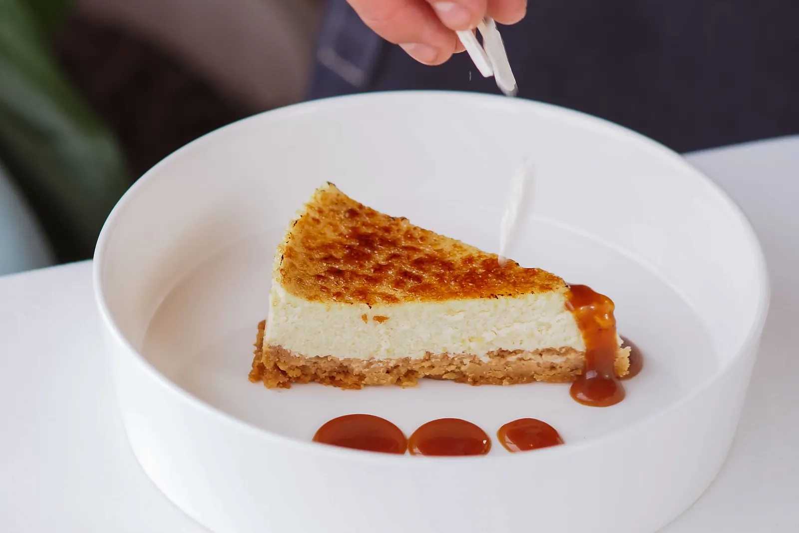 A slice of cheesecake with a deeply browned top, drizzled with caramel sauce