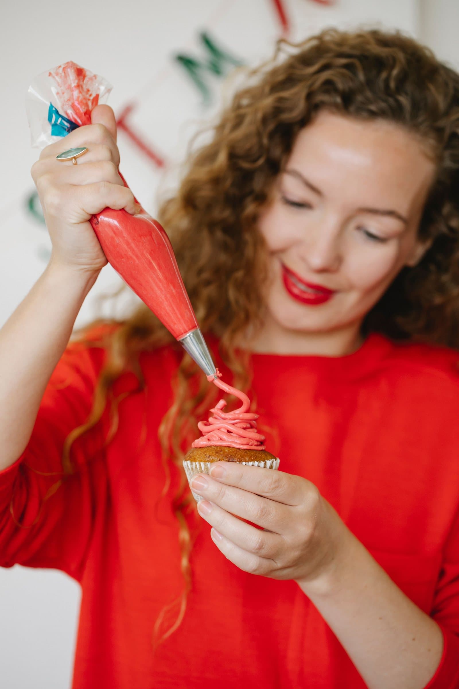 A hand piping pink buttercream in a swirl onto a cupcake
