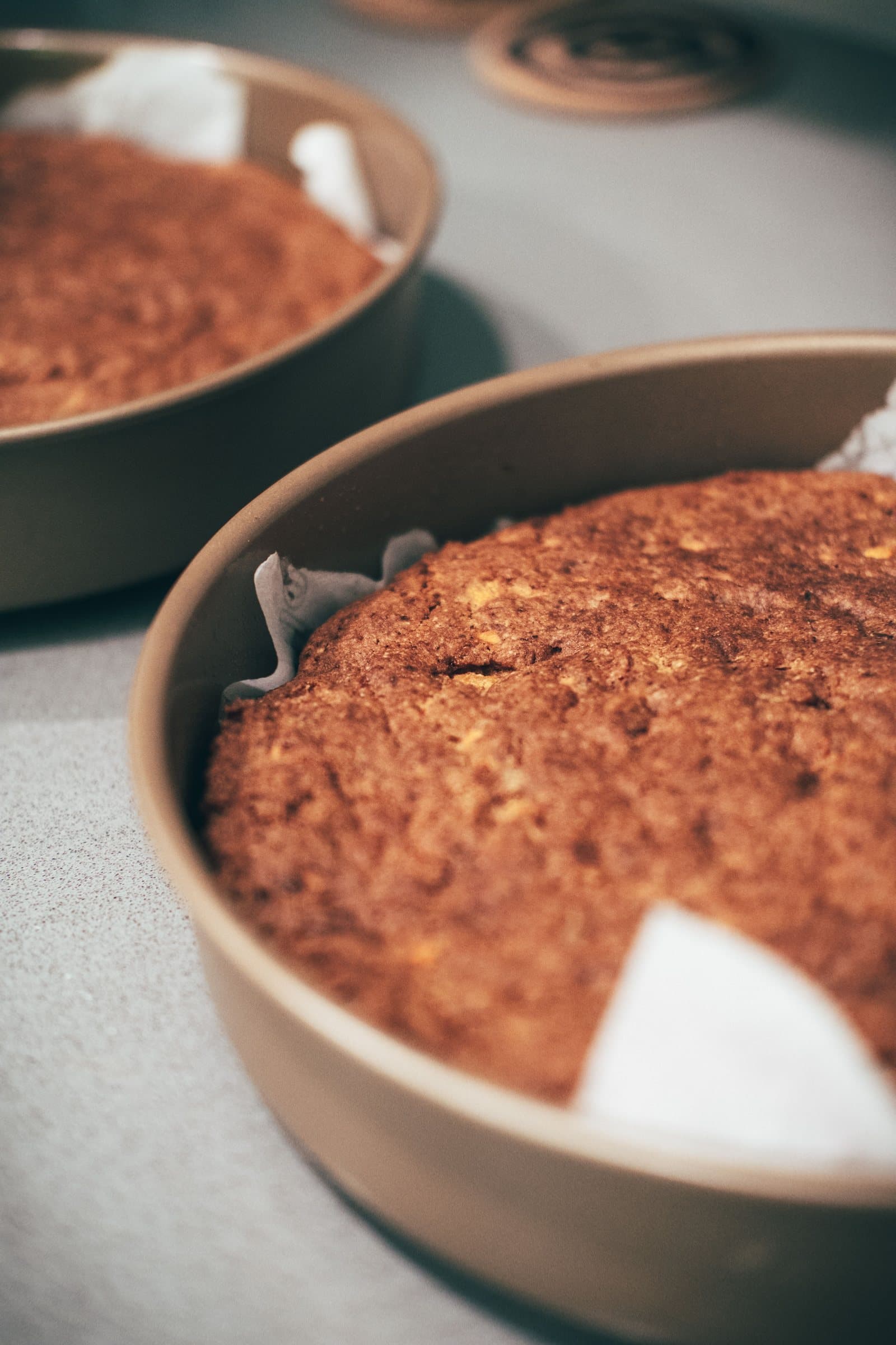 Two round cakes cooling in parchment-lined metal baking pans side by side