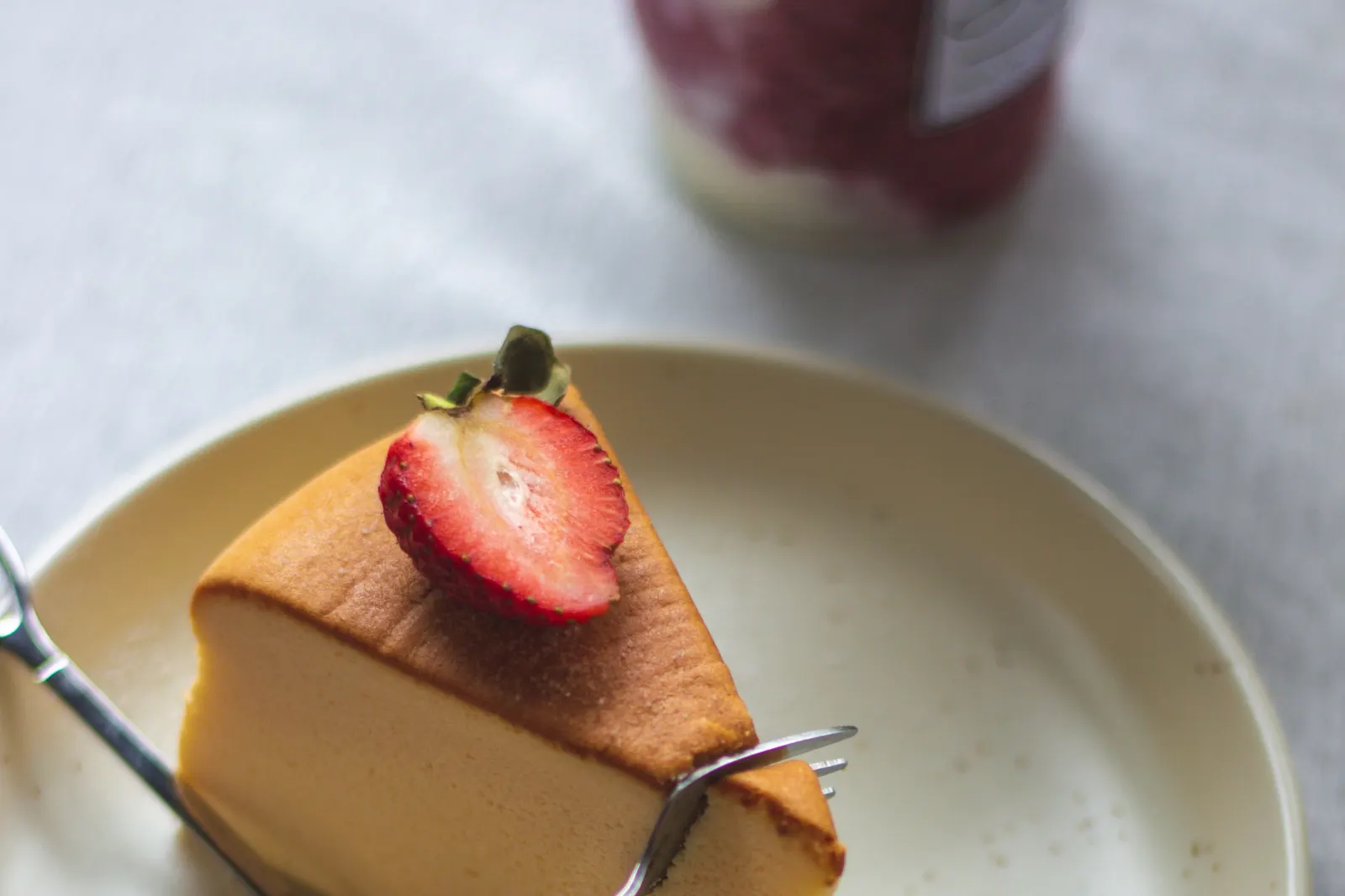 A fork slicing into a cheesecake topped with a fresh strawberry