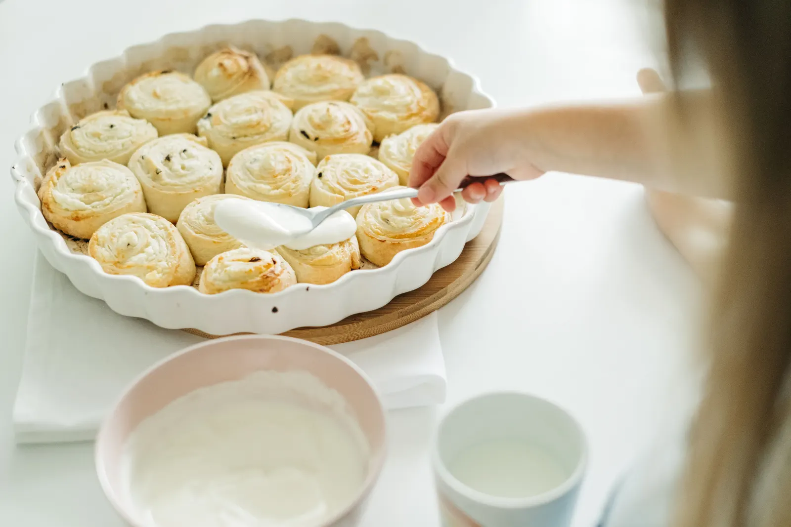 A child spreading icing over freshly baked cinnamon rolls