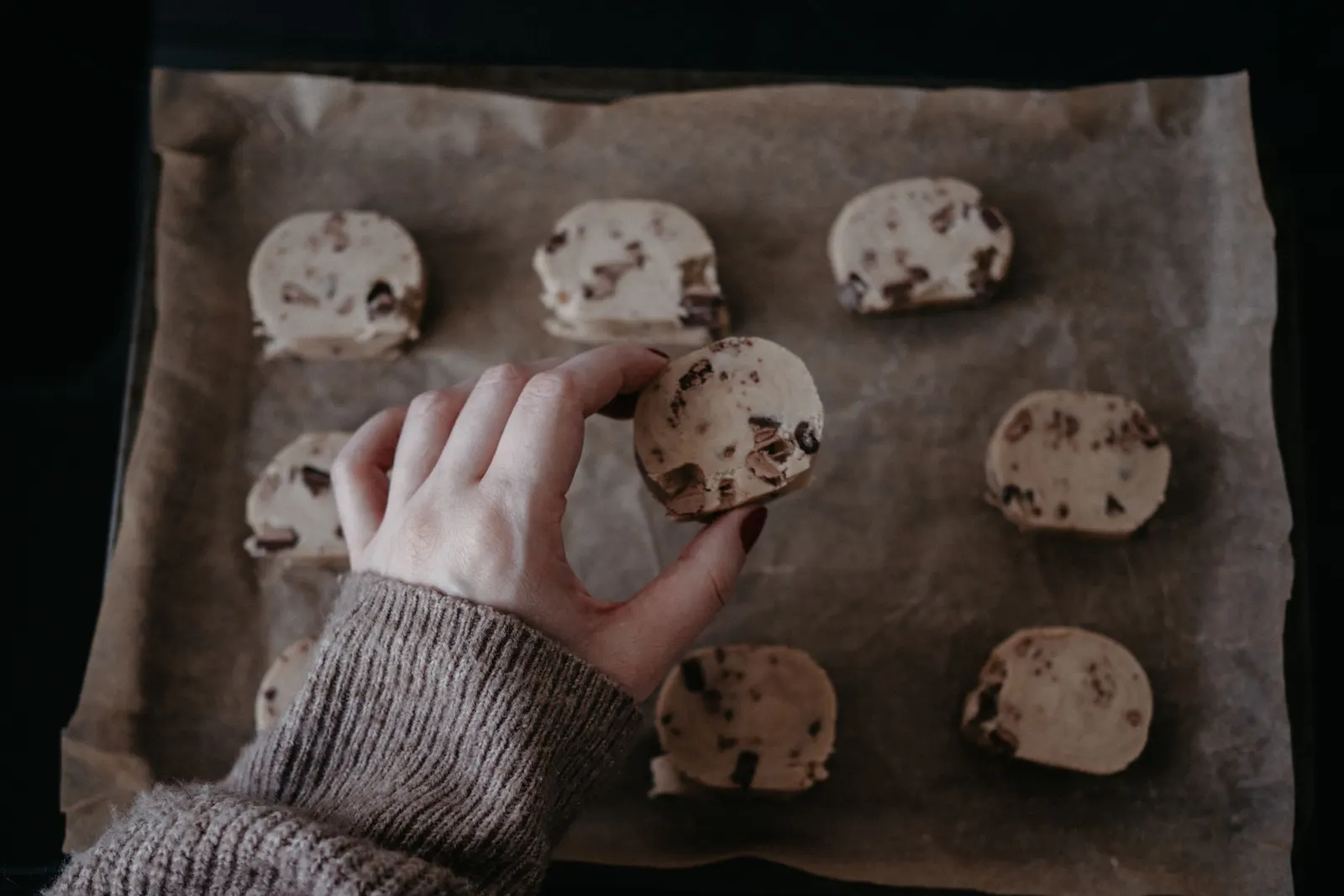 A hand placing a ball of cookie dough onto a lined baking sheet