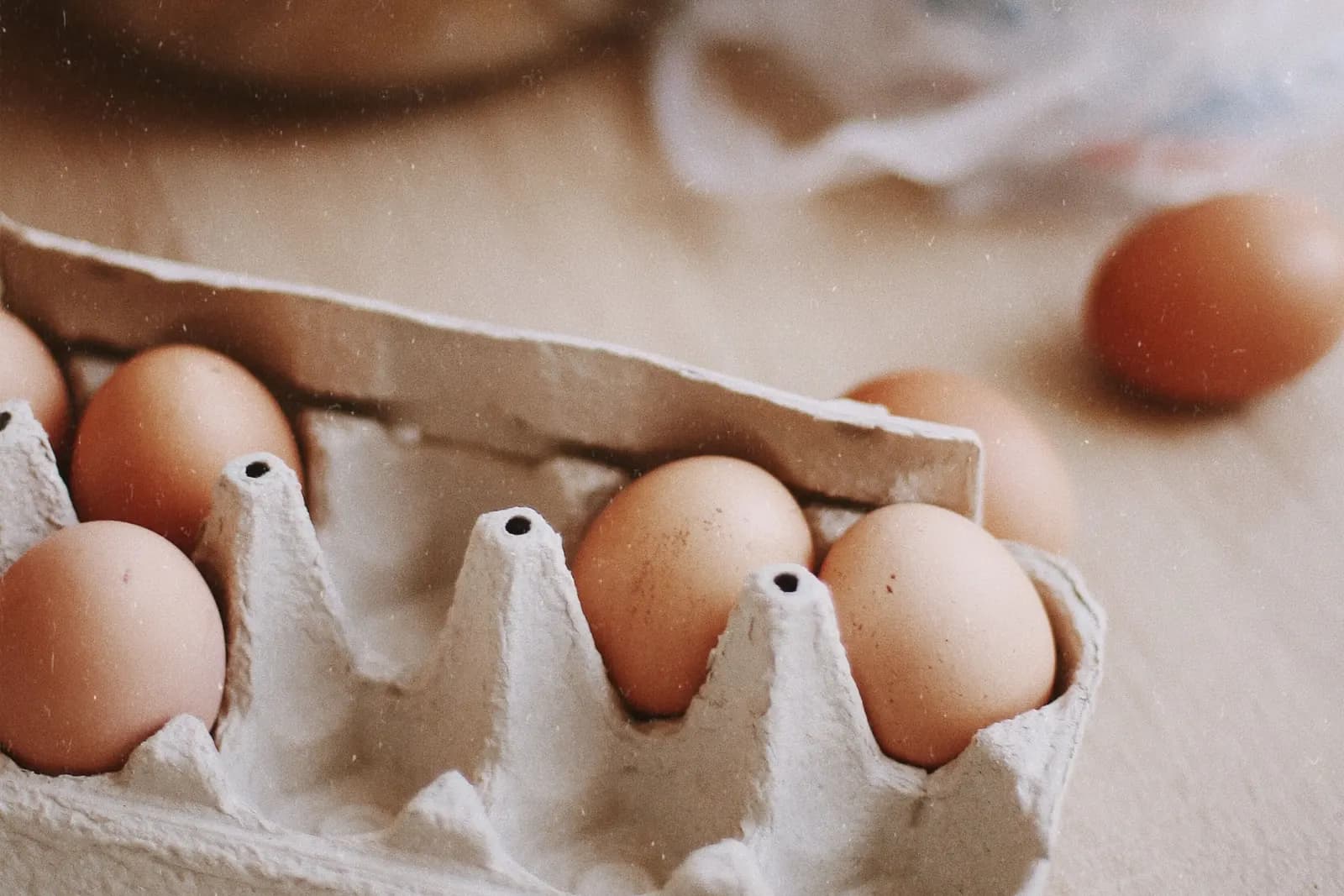 A carton of fresh eggs next to a bowl of flour on a kitchen counter