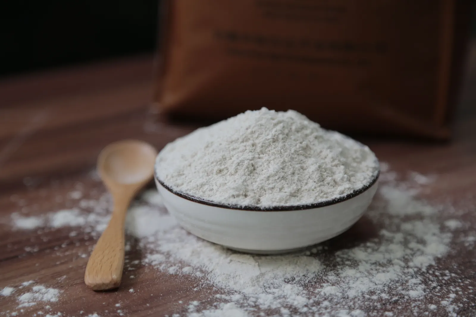 Flour in a ceramic bowl with a wooden spoon