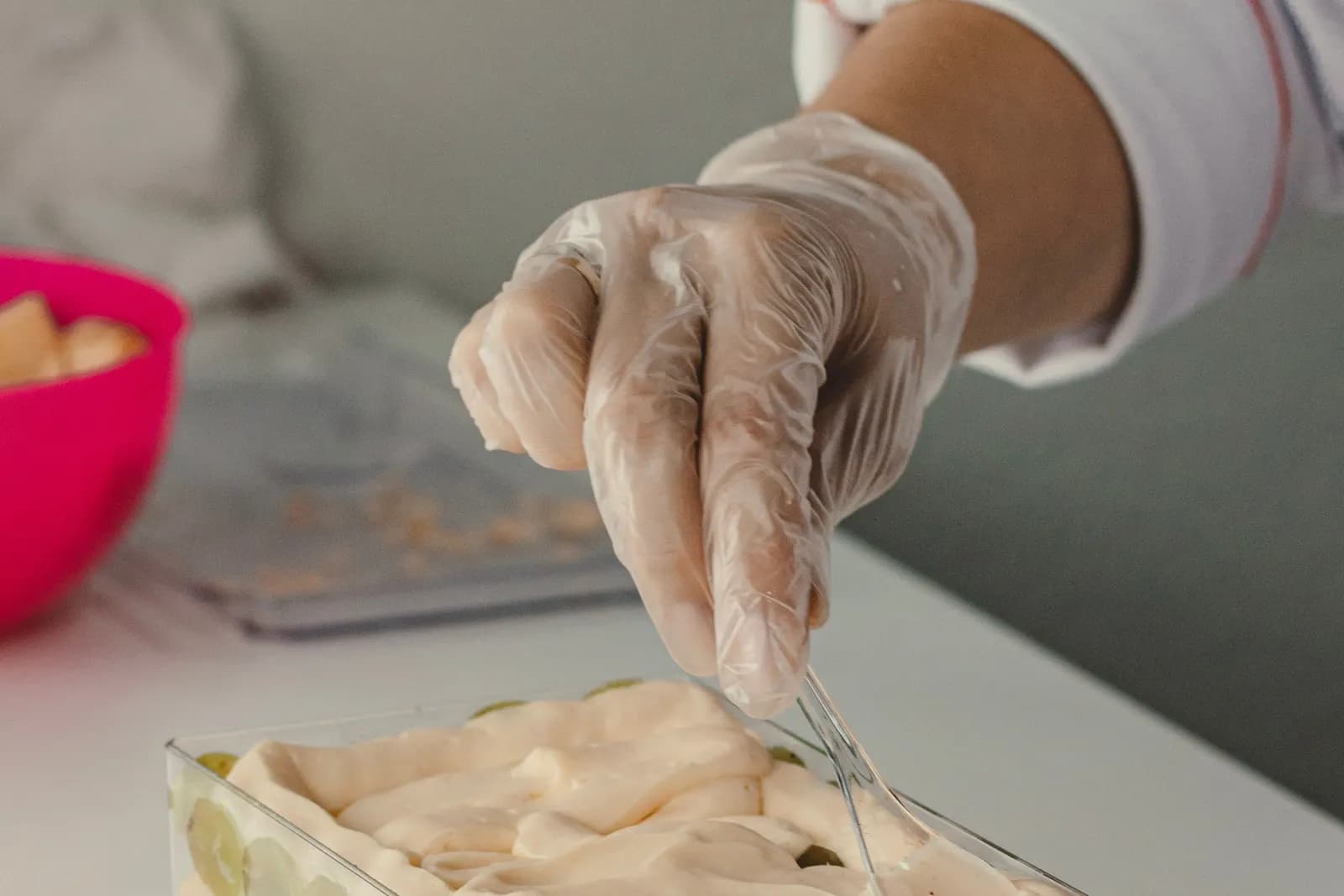 A baker's hands layering a chilled dessert with cream and grapes