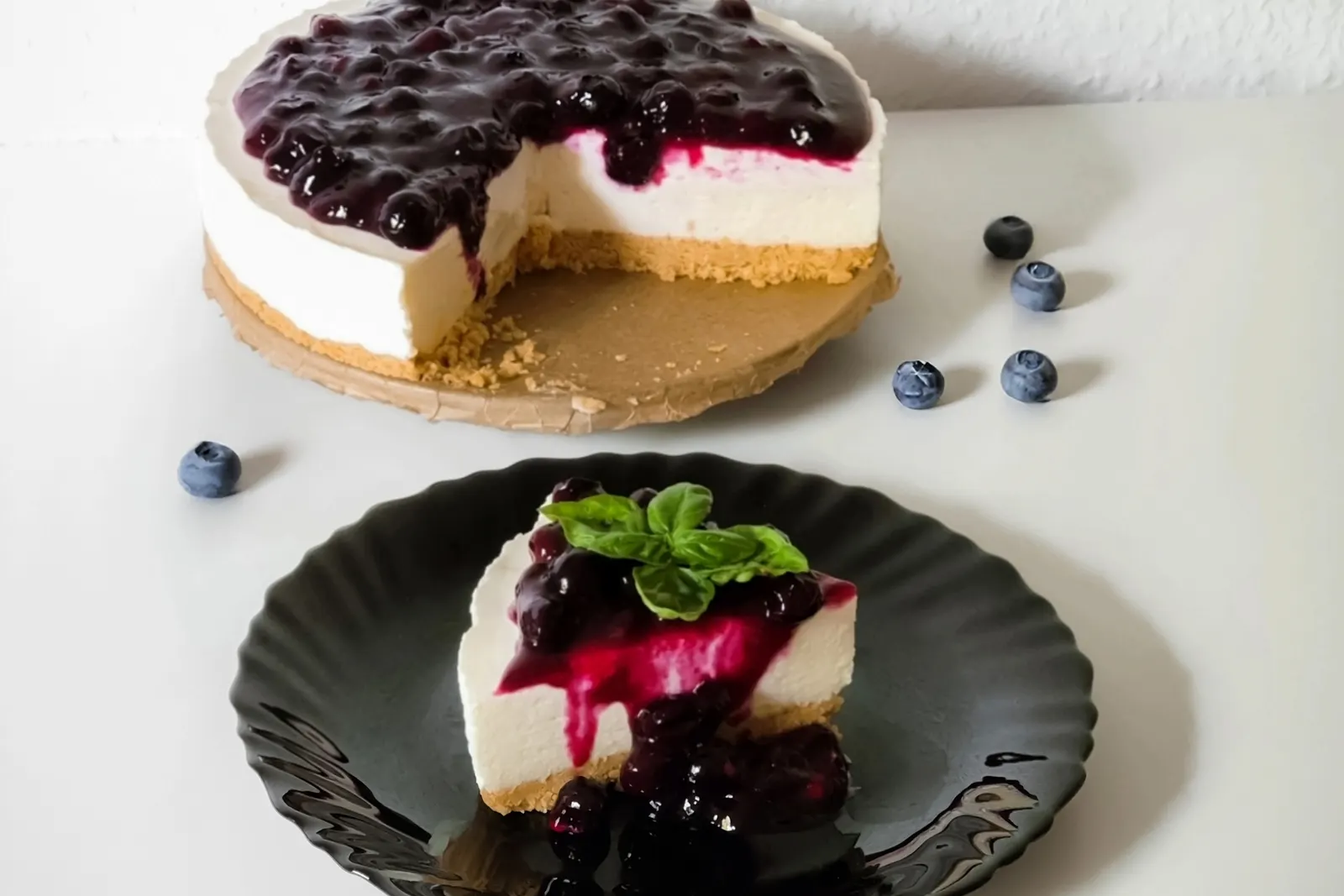A sliced no-bake blueberry cheesecake with a biscuit crust, served with fresh blueberries