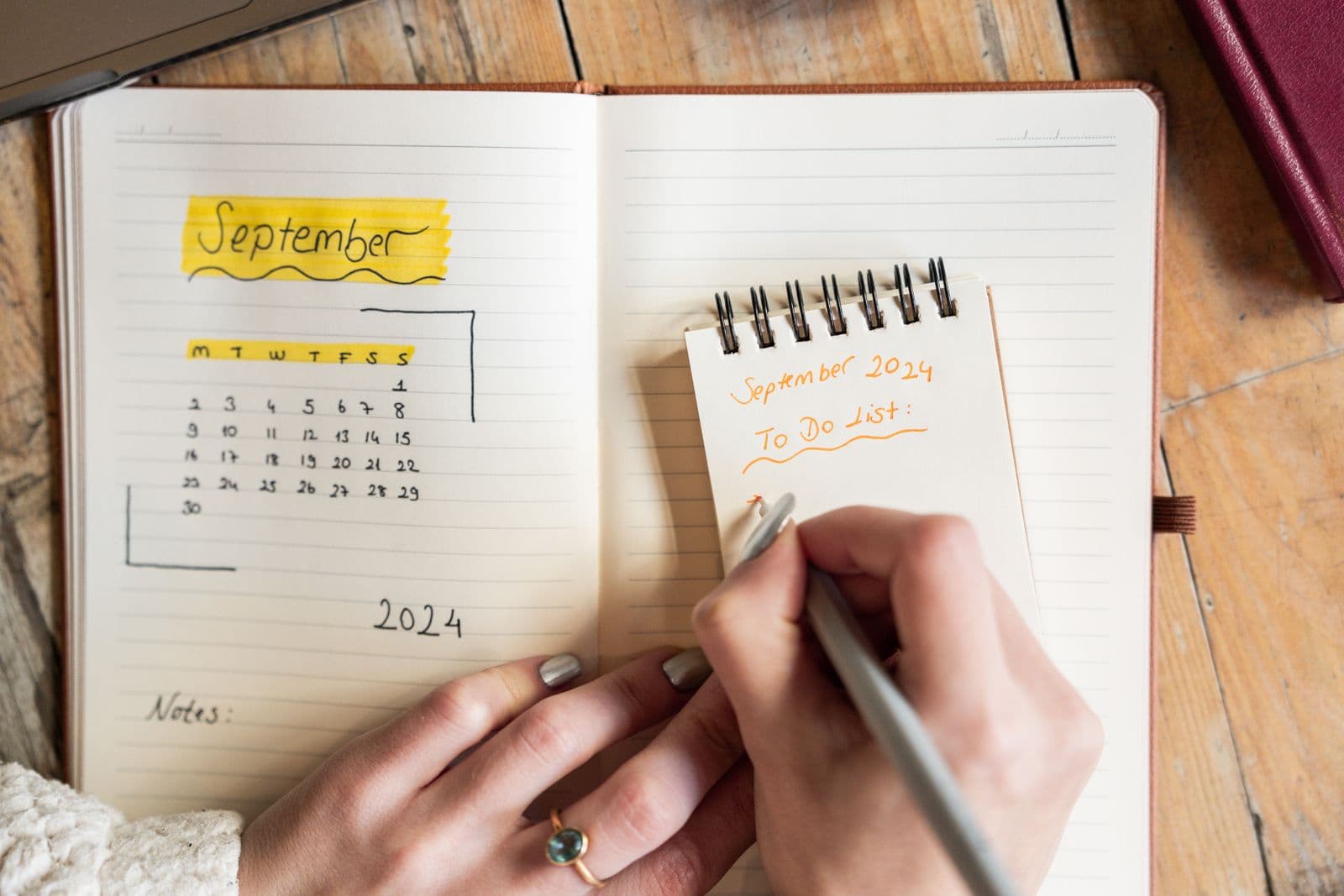 An overhead view of hands writing a 'To Do List' on a notepad next to an open planner showing a September calendar