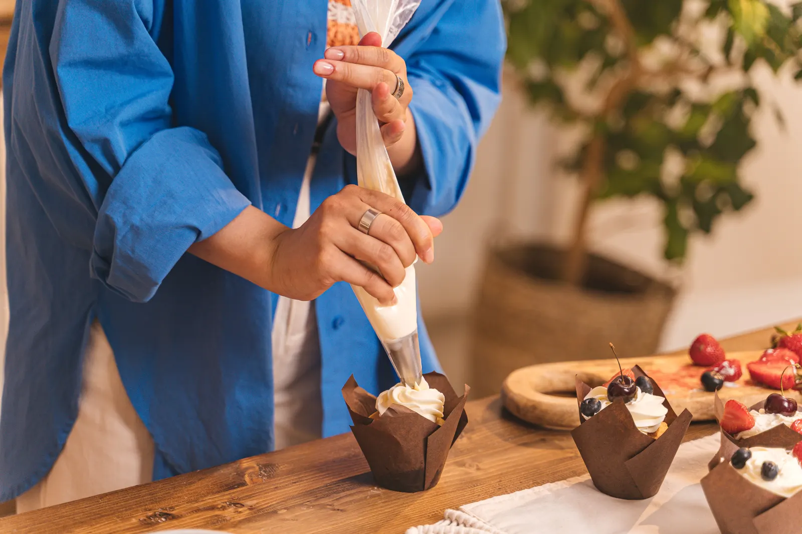 A hand piping icing onto a cupcake with a piping bag