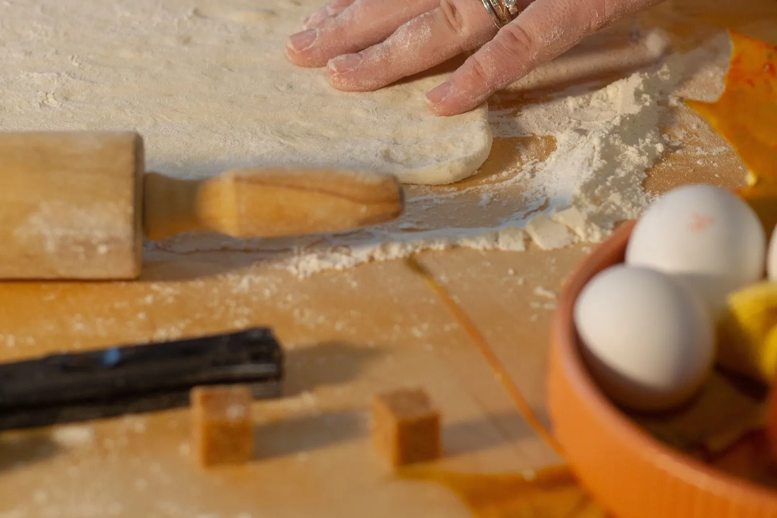 Hands rolling out pie dough with a rolling pin on a wooden table