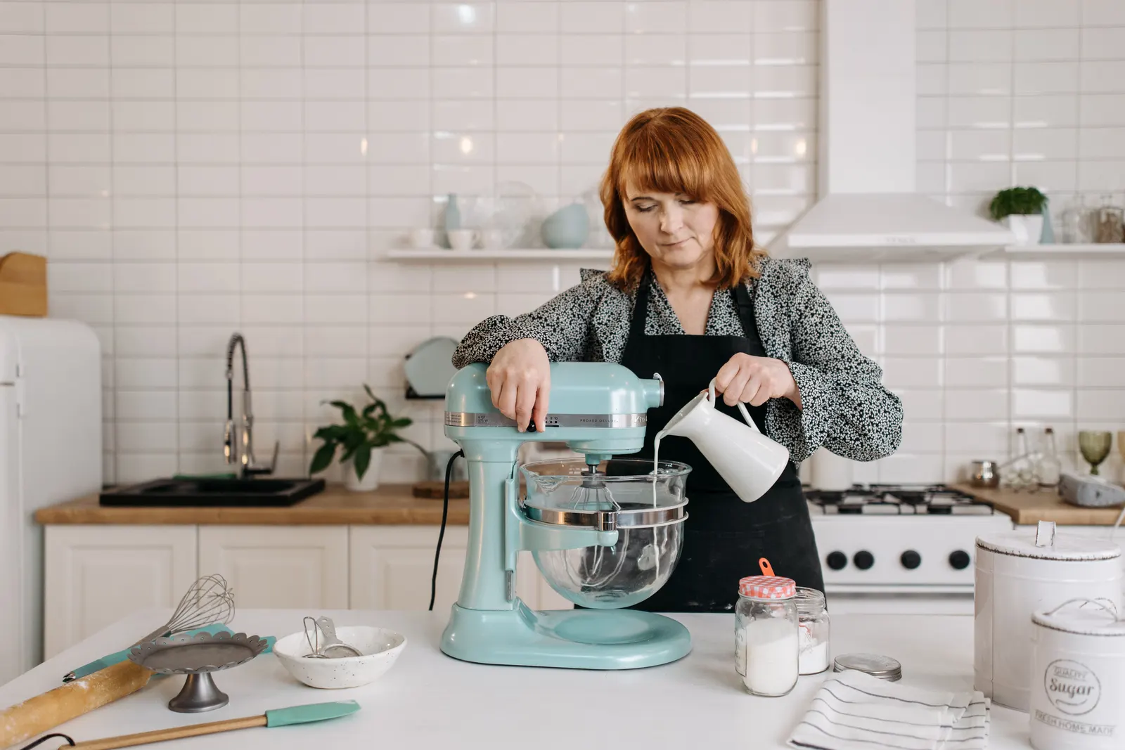 A woman pouring milk into a stand mixer while preparing dough