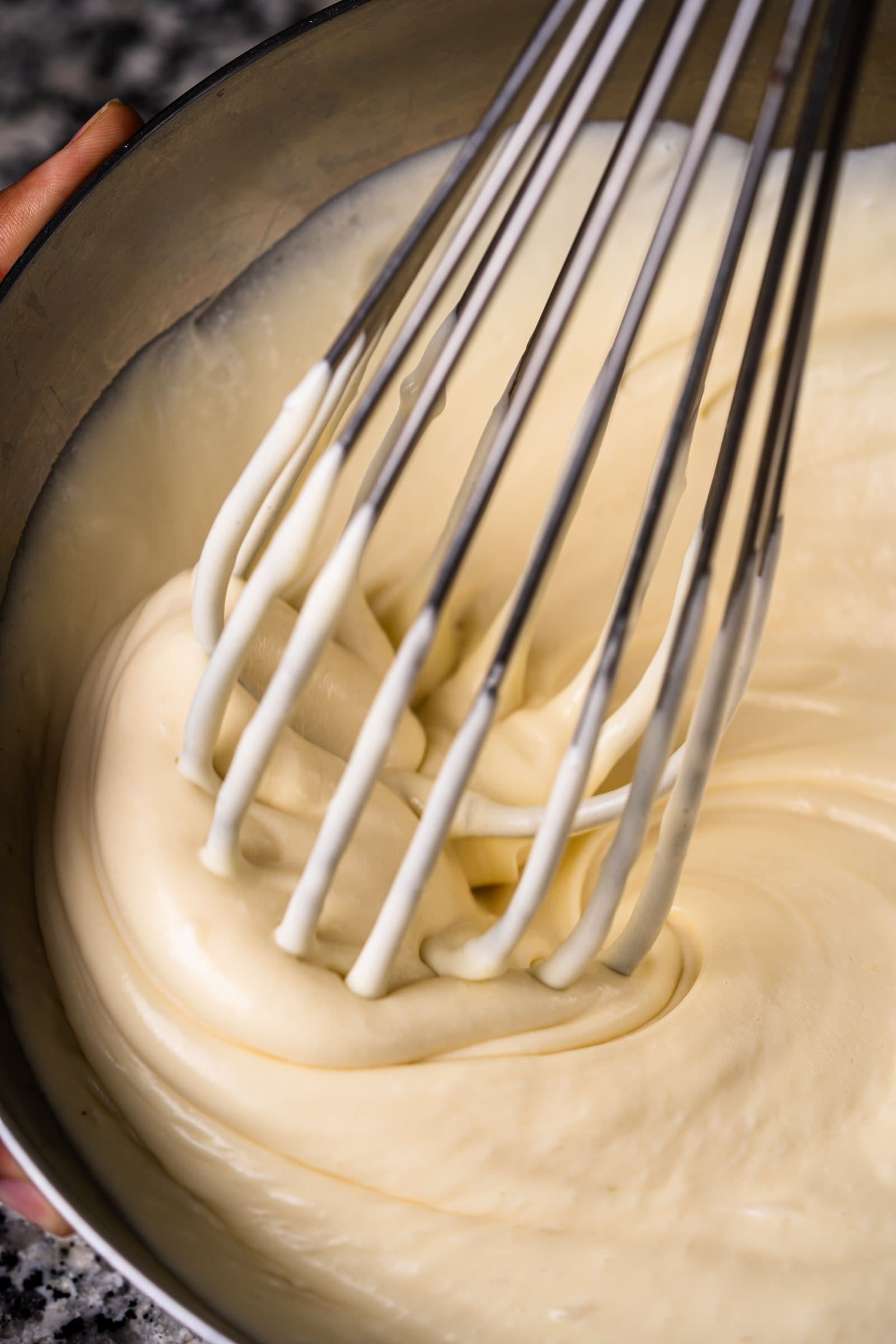 A metal whisk lifting pale, smooth cake batter in a mixing bowl