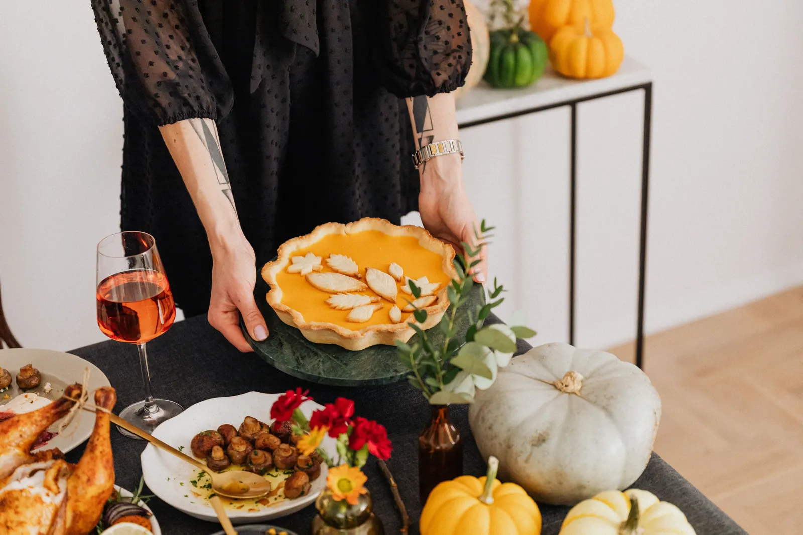 A woman presenting a pumpkin pie decorated with pastry leaves at a Thanksgiving table